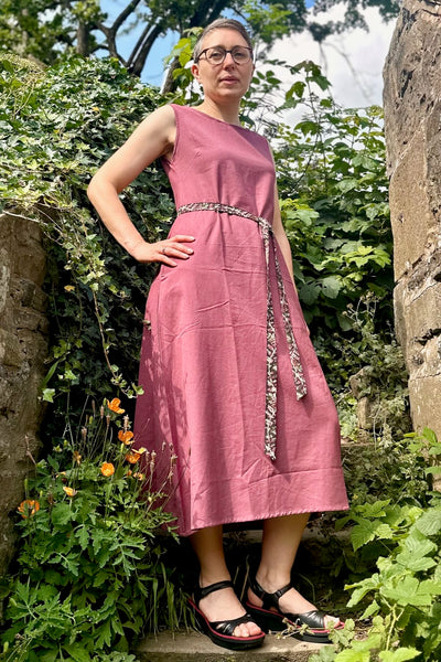 Woman in a pink dress standing in a garden with greenery and flowers.